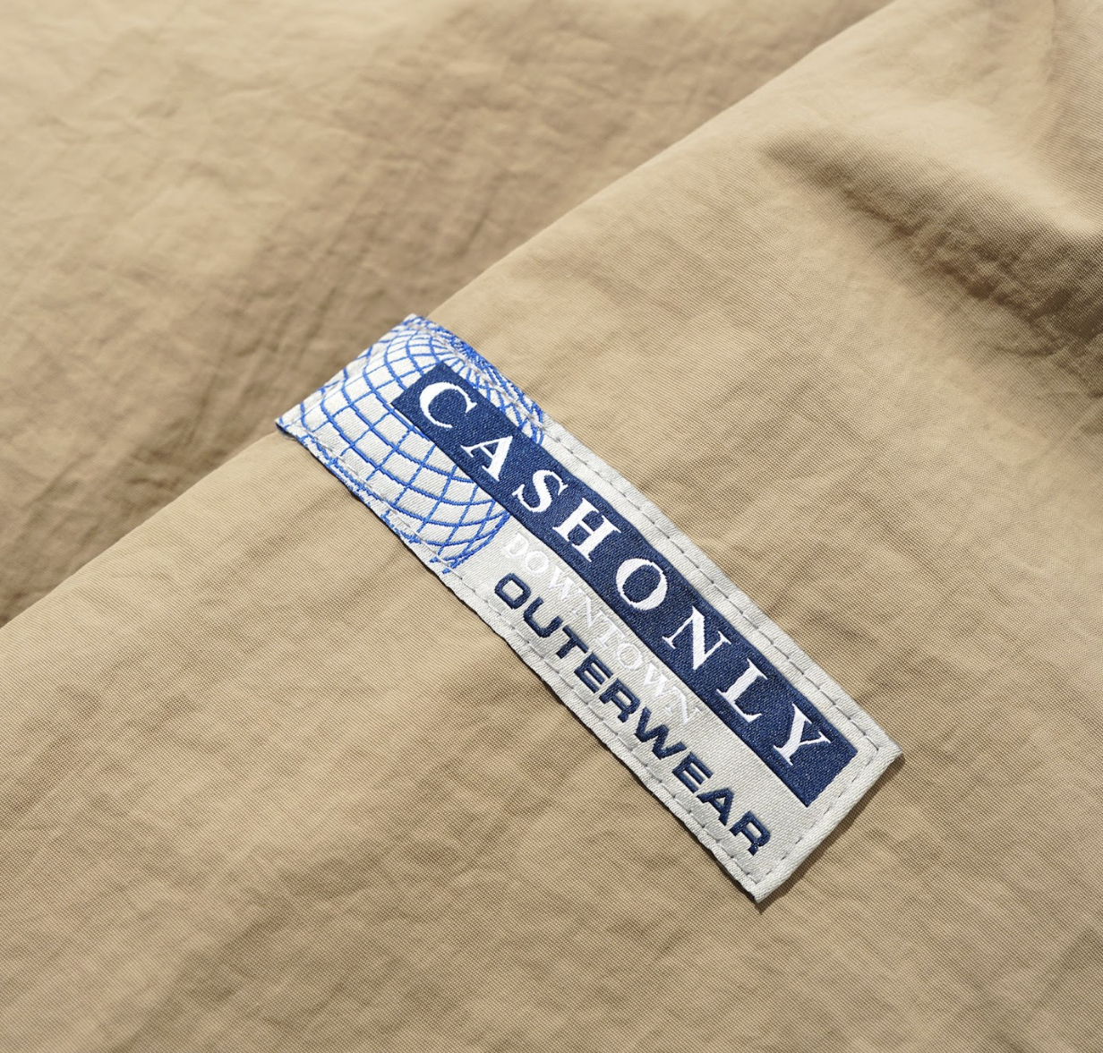 Close-up of a 'CASHONLY OUTERWEAR' label on beige fabric.