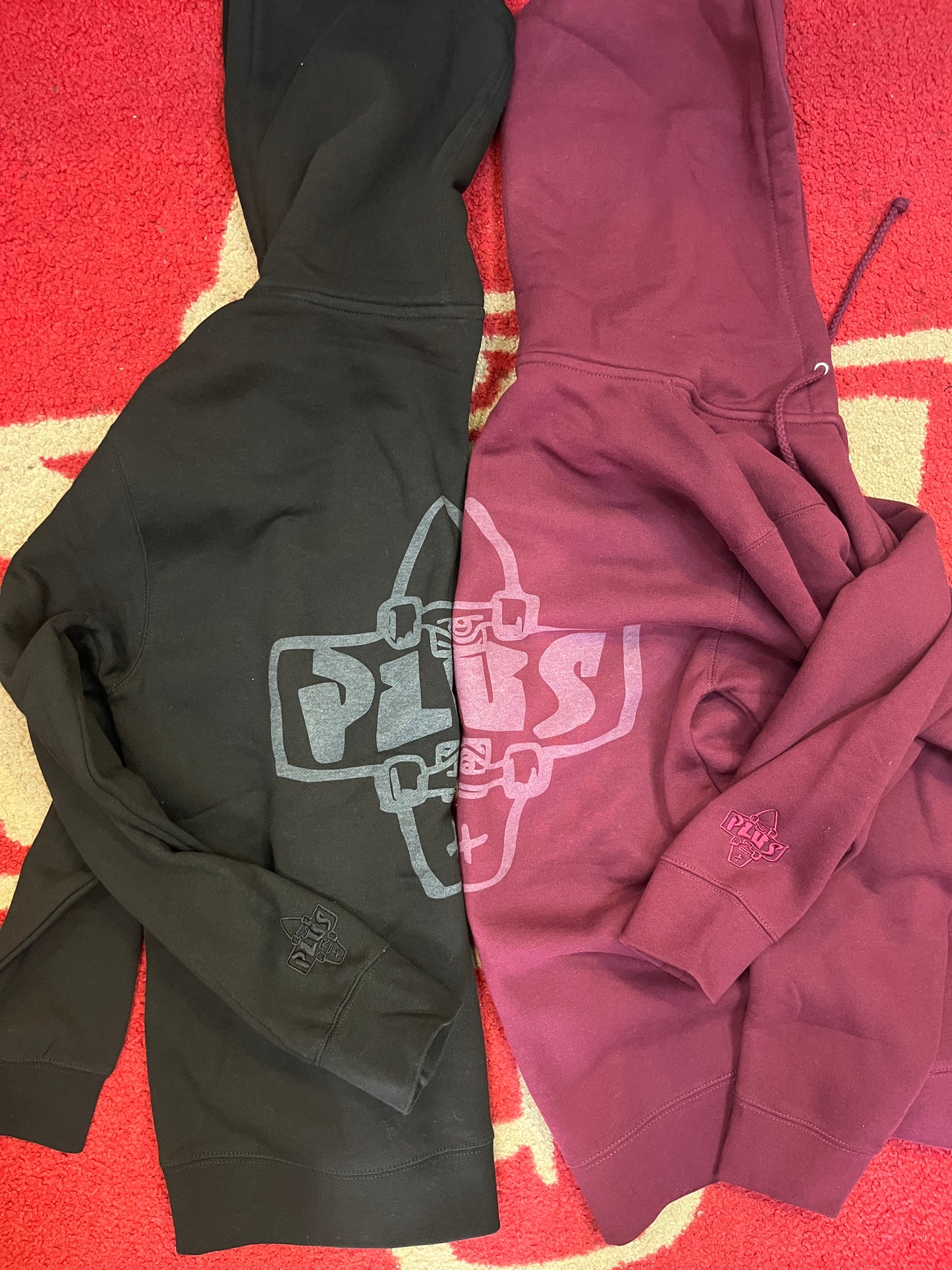 Folded maroon and black hoodie with graphic design on a red and yellow patterned surface