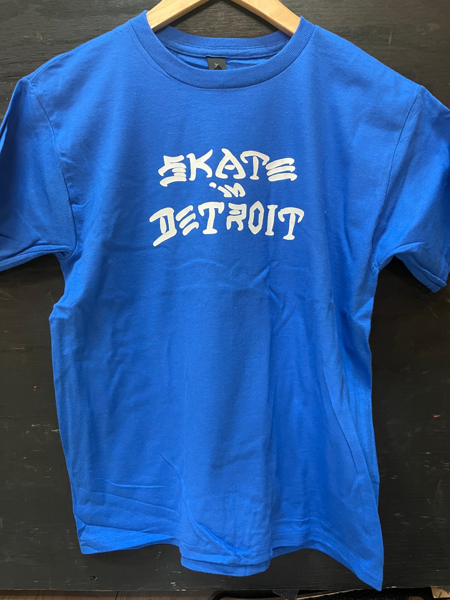 Blue t-shirt with 'Skate Detroit' text on a black surface