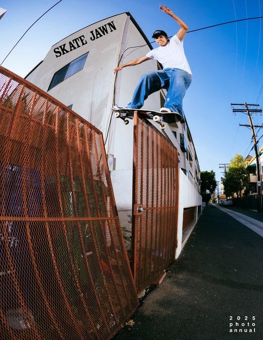 Person skateboarding on a trailer with 'SKATE JAWN' branding under a clear blue sky.
