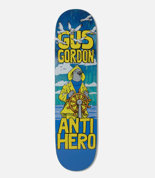 A skateboard deck featuring a graphic design with the text 'GUS GORDON' at the top and 'ANTI HERO' at the bottom. The illustration shows a pigeon in a yellow raincoat steering a ship's wheel against a blue sky with clouds.