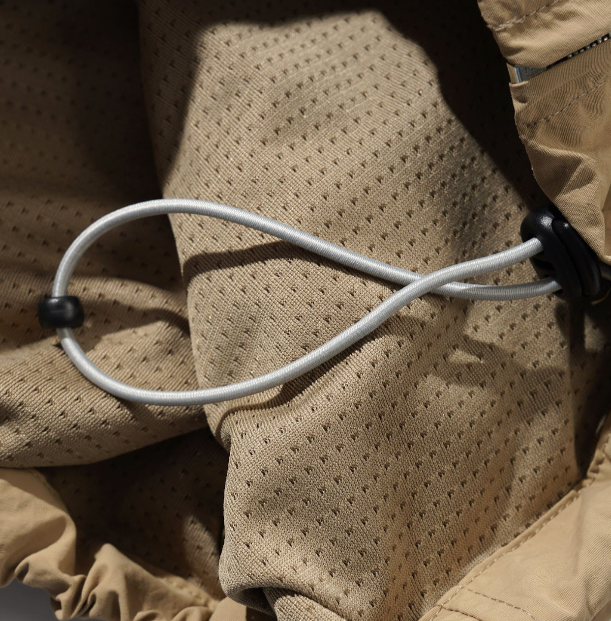 Close-up of a beige jacket with a white cord and black buttons.