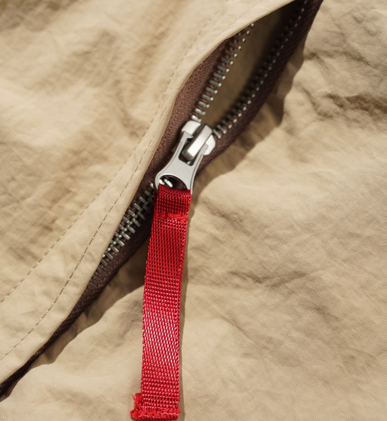 Close-up of a beige jacket with a red zipper pull.