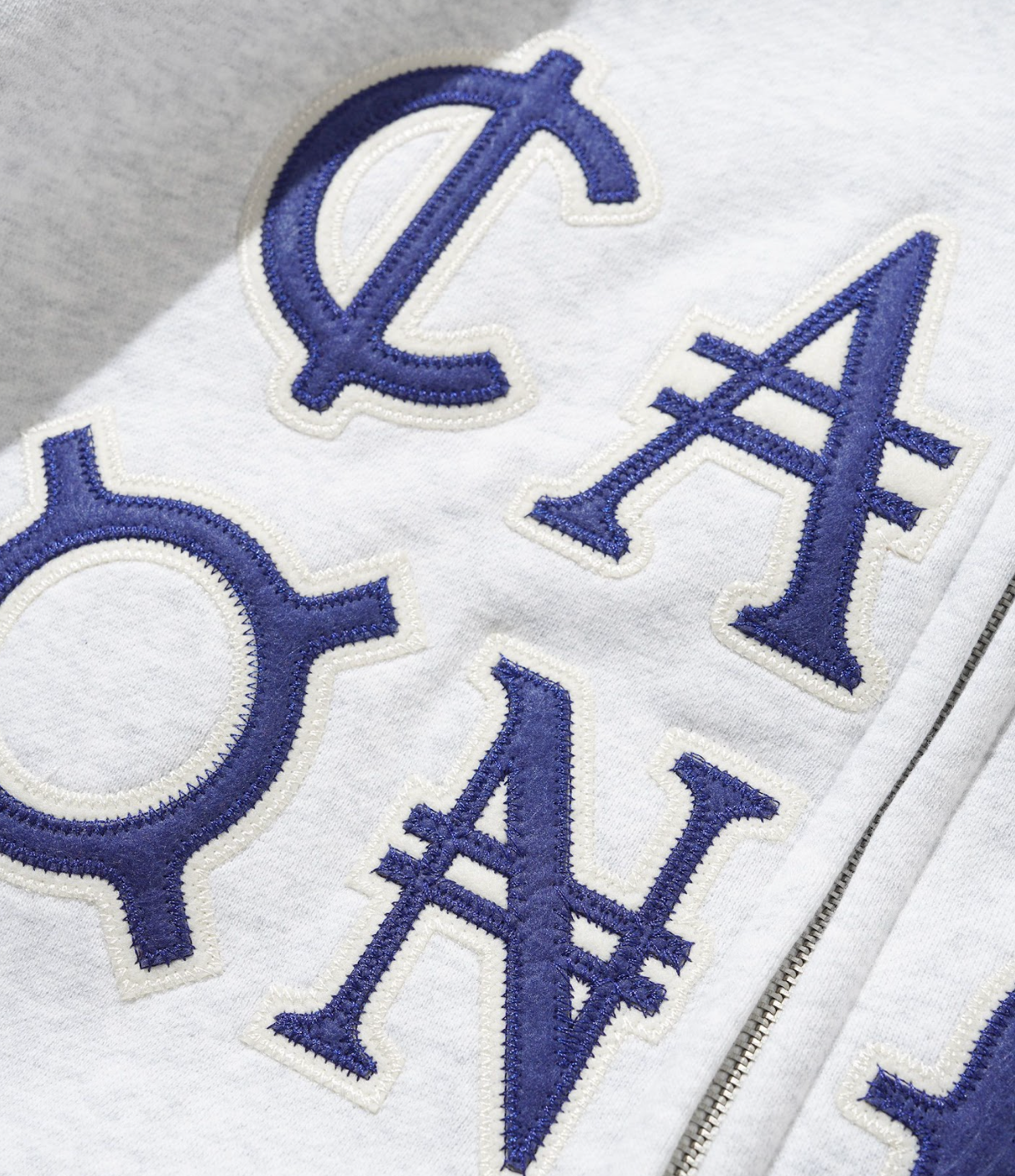 Close-up of a white jacket with blue embroidered letters on a gray background