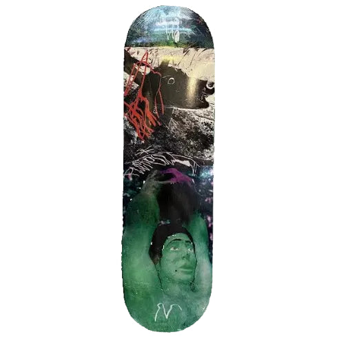 A skateboard with a highly detailed, colorful graphic print lies on a light-colored wooden floor. The graphic features a green face with a black beanie, red graffiti-style scribbles, and a dark abstract background.