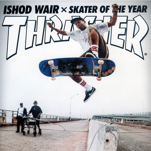 A skateboarder in midair performing a trick over a bridge, with large 'Thriver' text and the words 'Ishod Wair x Skater of the Year' across the top. Two men push a cart in the background on the bridge.