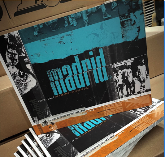 Stack of books or magazines with 'Madrid' and '50 Years of Skateboarding' text on a cardboard surface.