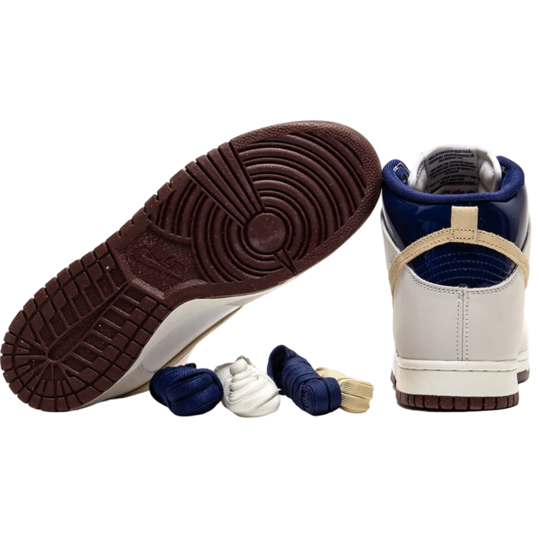 A pair of high-top sneakers shown on a white background, with one shoe turned upside down to display the dark brown textured sole and the other standing upright to show the side and heel. The shoes feature a white leather upper, navy blue overlays, and beige accents, with matching navy and white shoelaces and a beige lace tip resting in front.