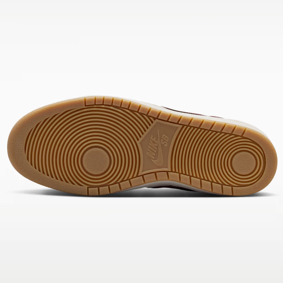 A close-up bottom view of a Nike sneaker showing its brown gum outsole with circular tread patterns and a visible embossed Nike Swoosh.