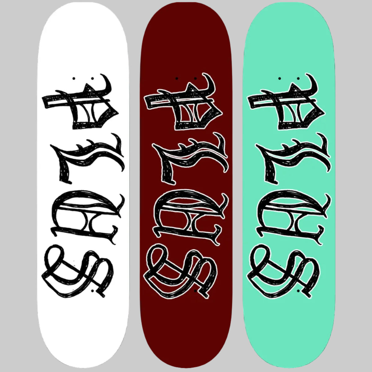 Three skateboard decks with black artistic designs on white, red, and green backgrounds.