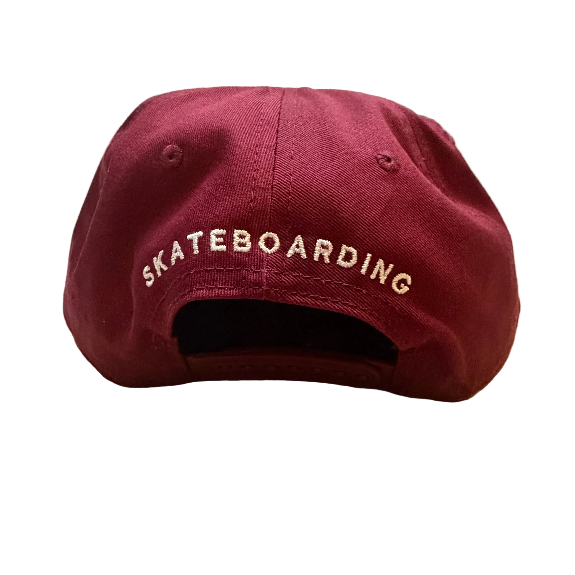 Maroon cap with 'SKATEBOARDING' text on a wooden surface