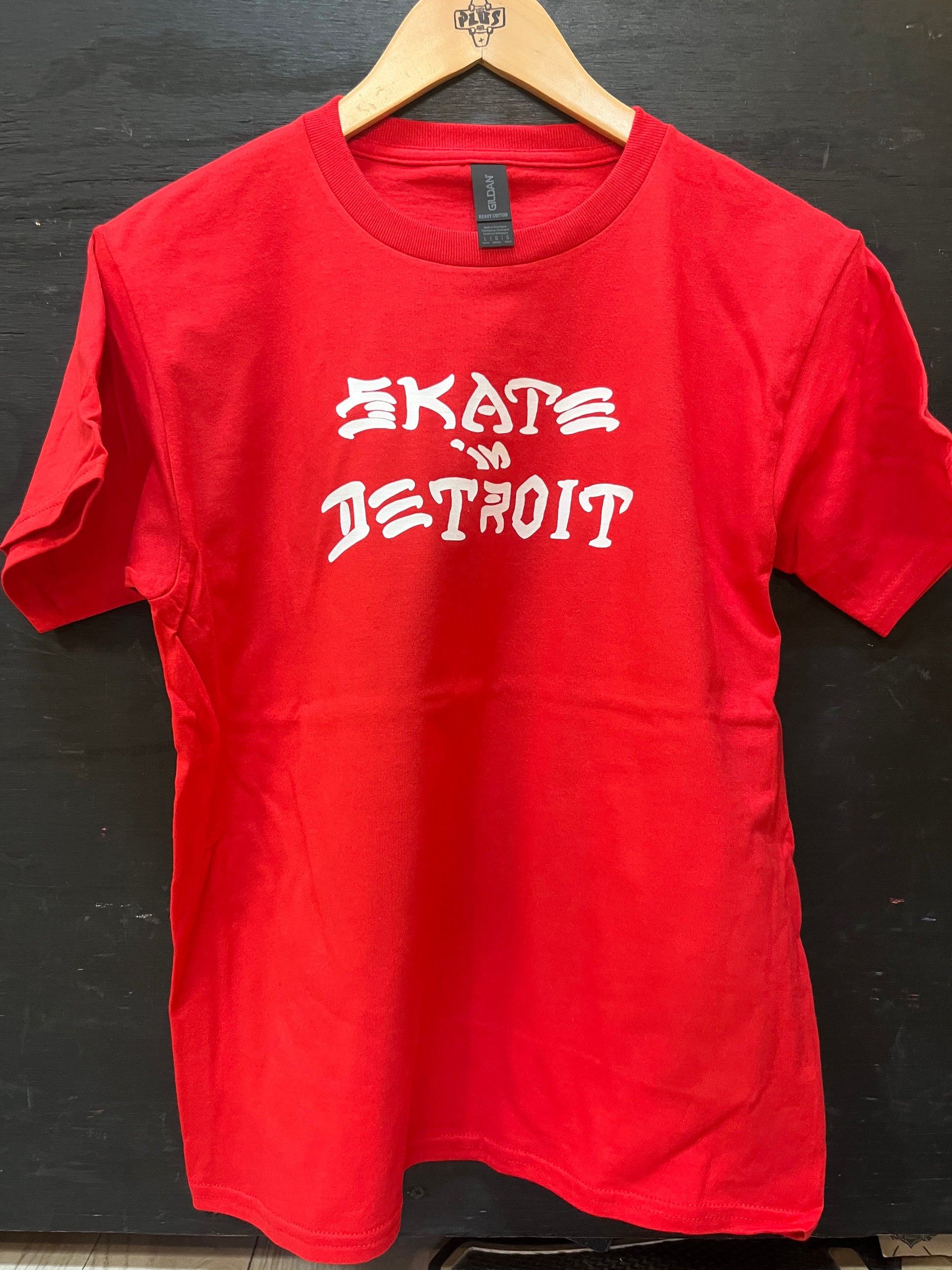 Red t-shirt with 'Skate Detroit' text on a wooden hanger against a dark background