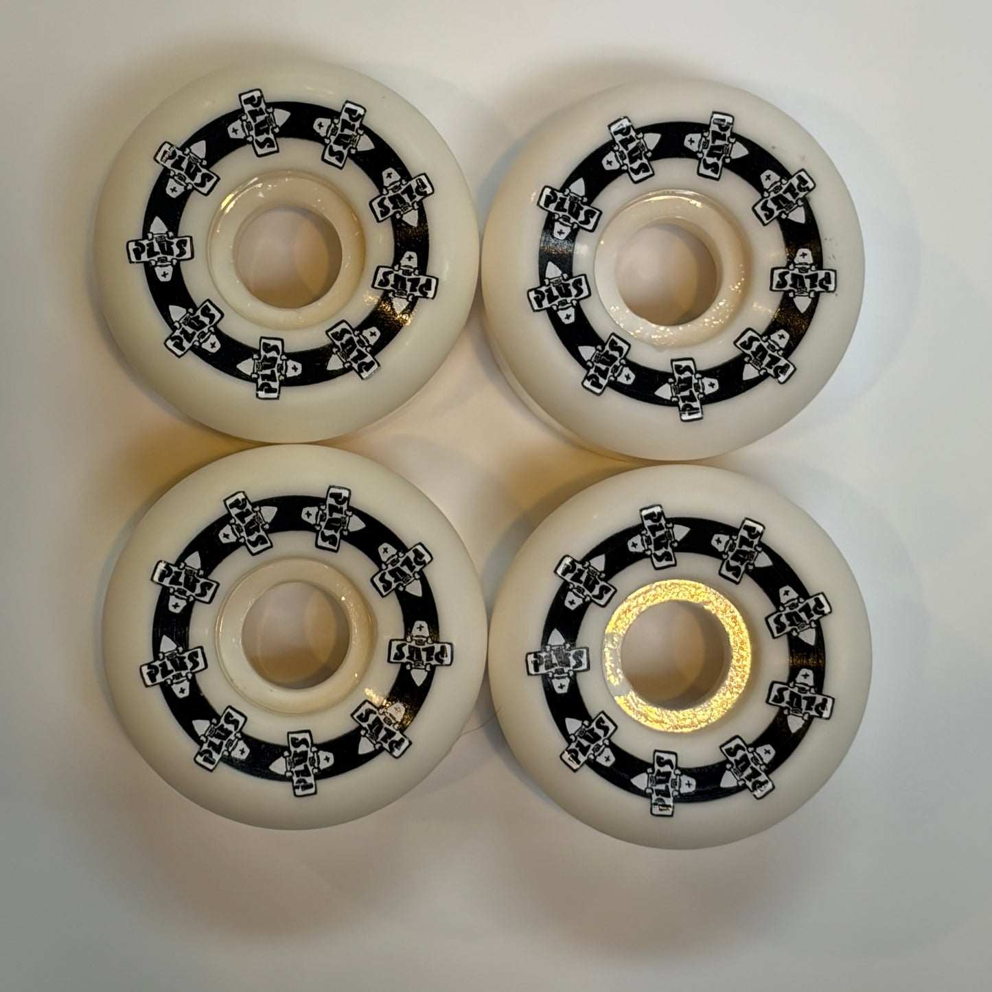Four white skate wheels with black bearings on a light gray background