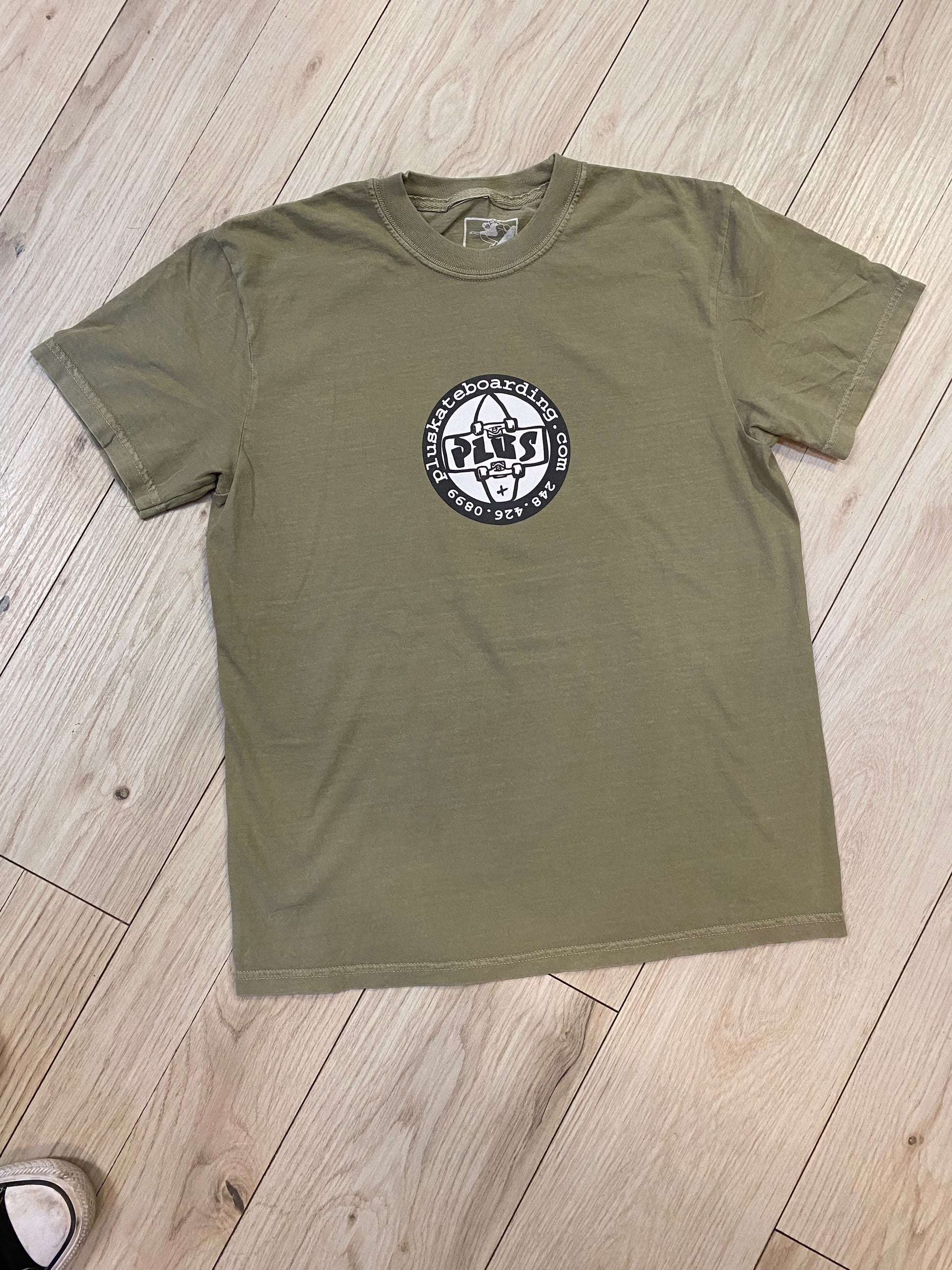 Green t-shirt with a logo on a wooden floor