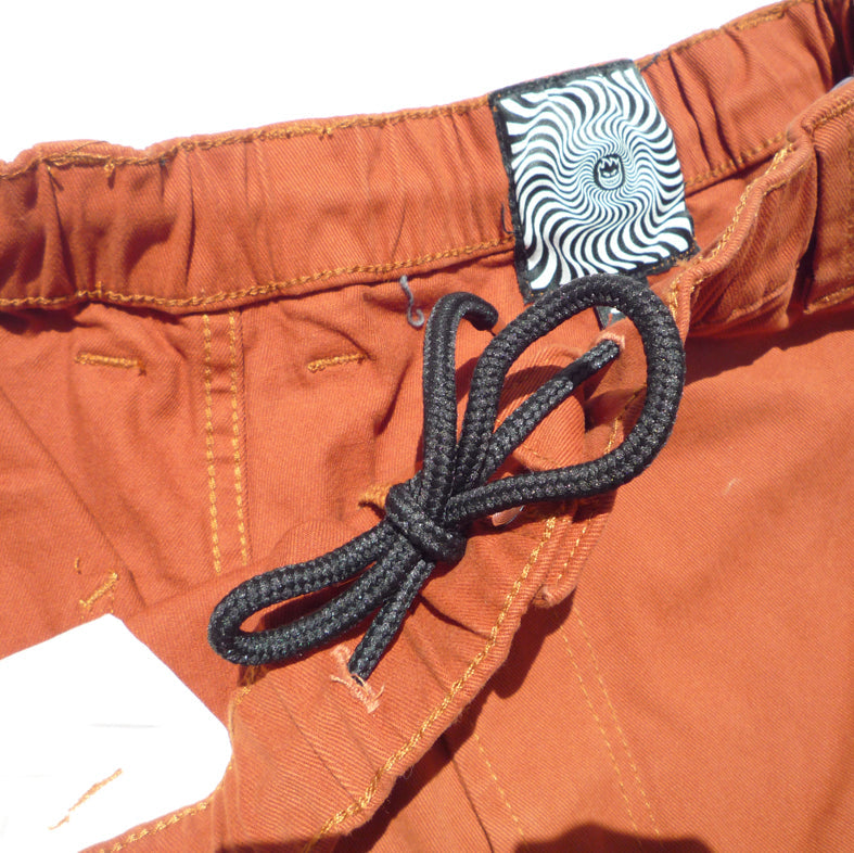 Close-up of orange pants with a black cord and patterned label.