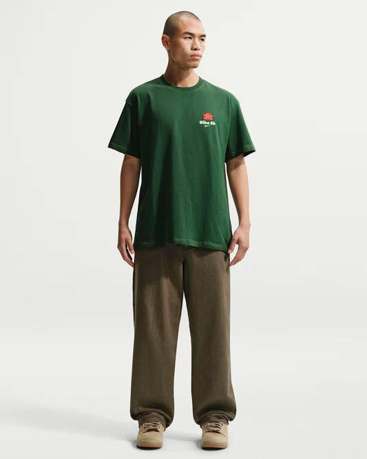 Man wearing a green t-shirt with a logo and brown pants on a white background