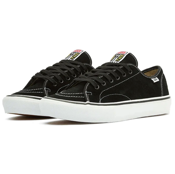 A pair of black suede low-top sneakers with white rubber soles, black laces, and a colorful logo patch on the tongue