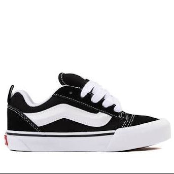 A classic low-top Vans sneaker in black and white, featuring a black canvas upper, white side stripe, white laces, and a white rubber sole, shown from a side profile view on a white background.