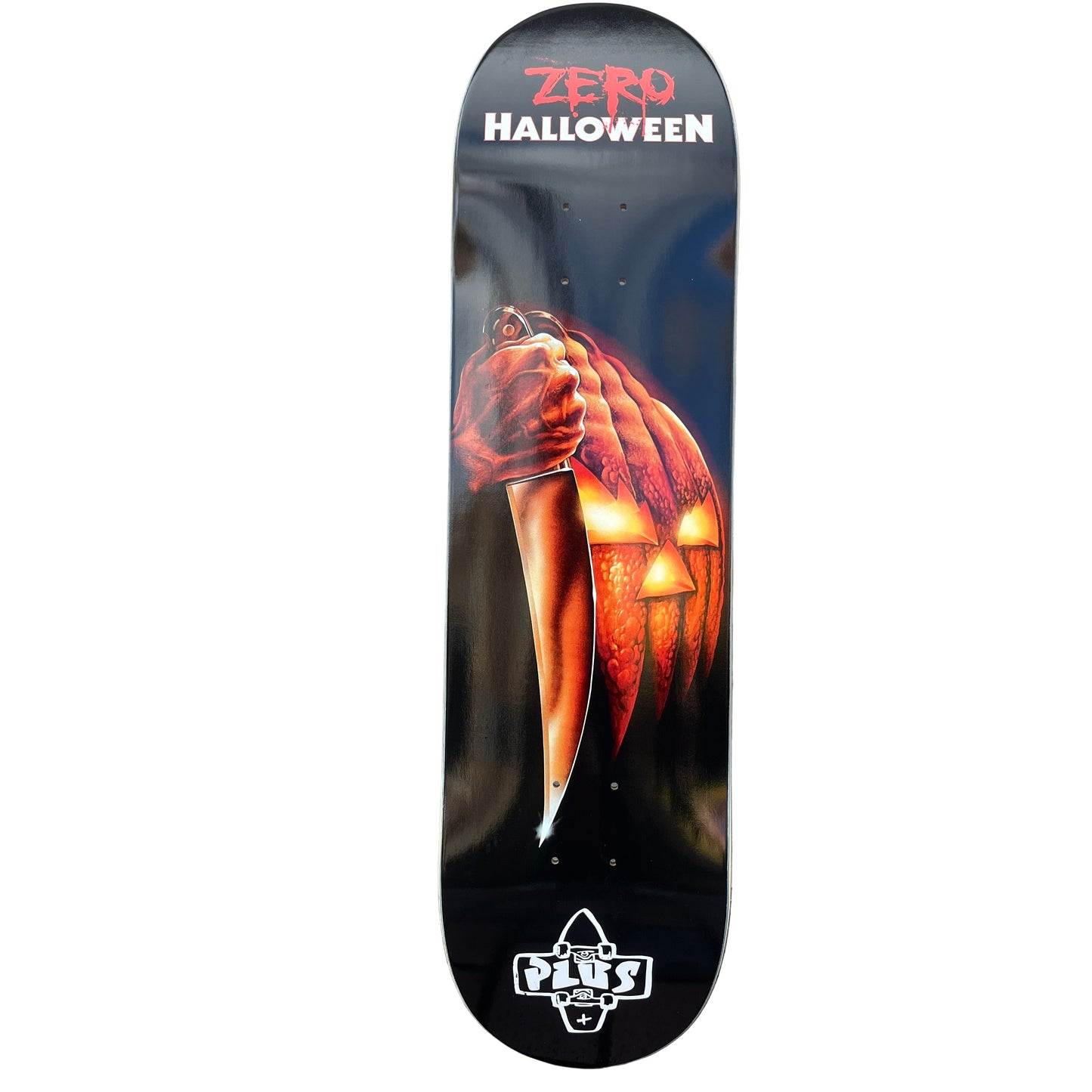 Skateboard deck with Halloween design featuring a hand holding a jack-o'-lantern against a gray wall.