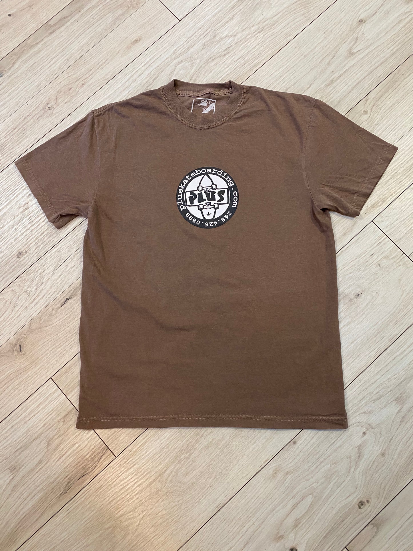 Brown t-shirt with a logo on a wooden floor
