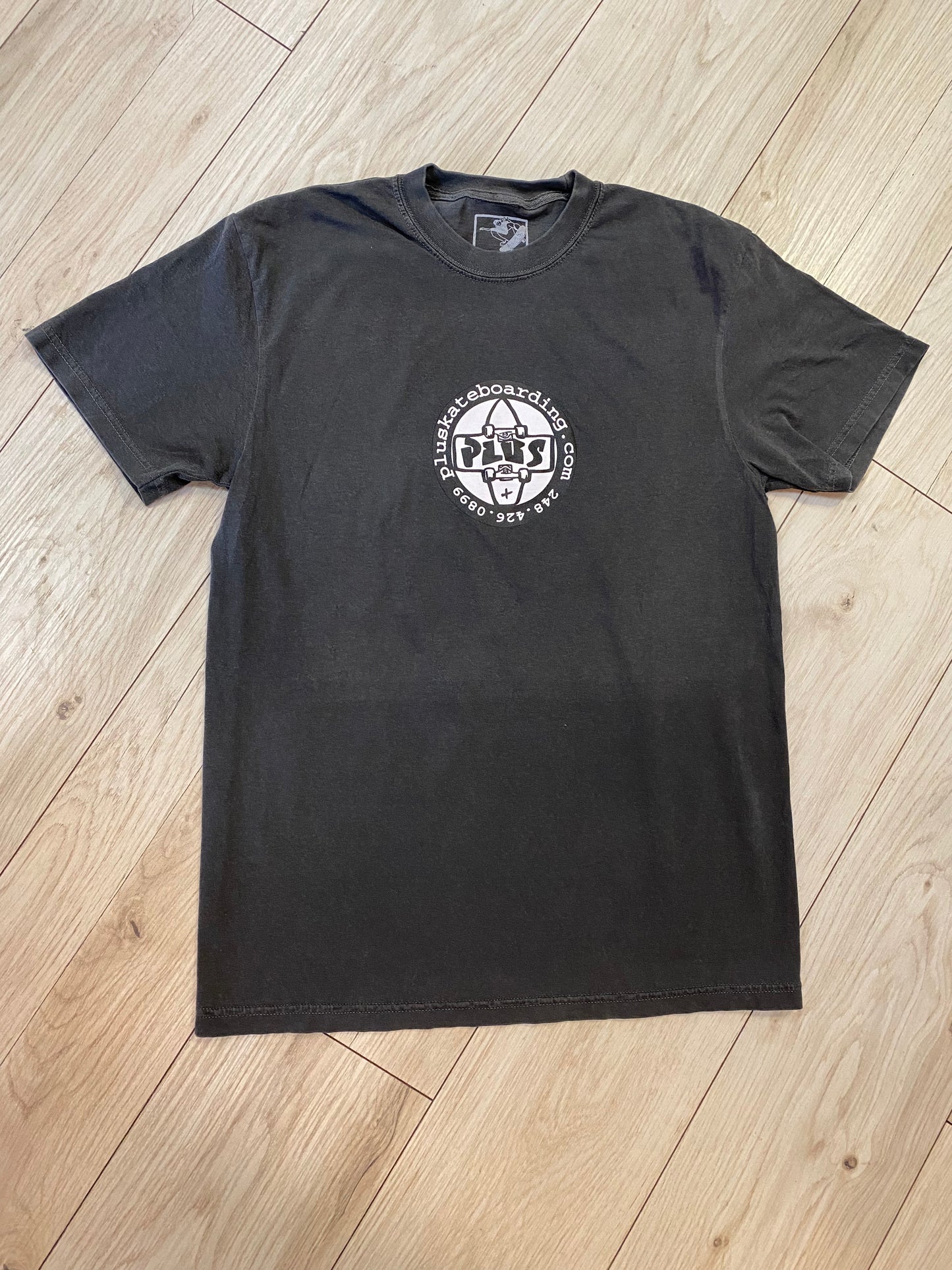 Black t-shirt with a logo on a wooden floor